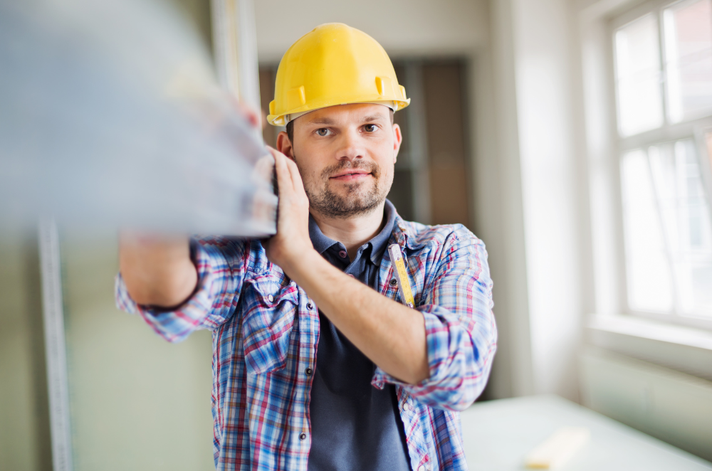 A construction worker with a hard helmet on, walking with a beam.