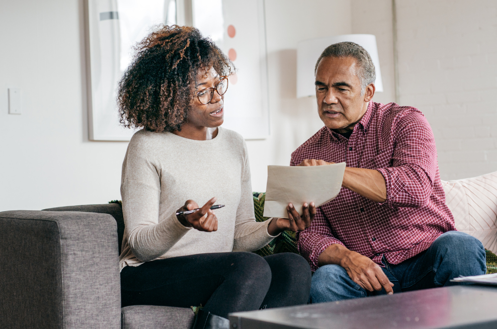 A couple sitting on a grey couch looking over their will.