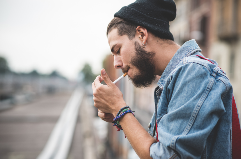 A man with a beanie hat lighting up a cigarette. Smoking cigarettes is not just bad for your health; additionally, it can be bad for your life insurance rate.