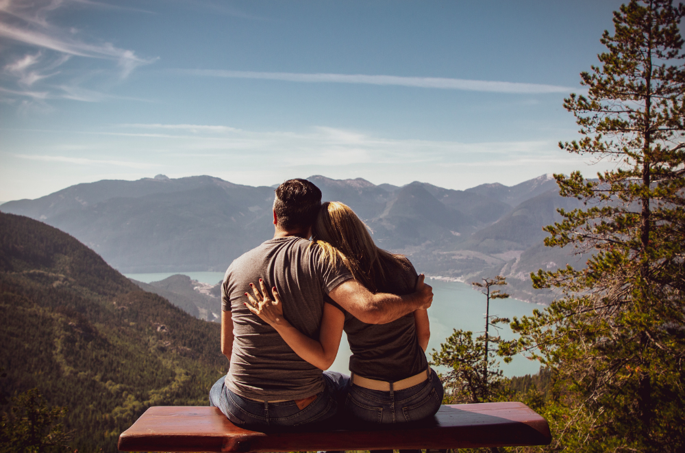 A couple sitting with their backs turned to the camera, overlooking a mountain valley.