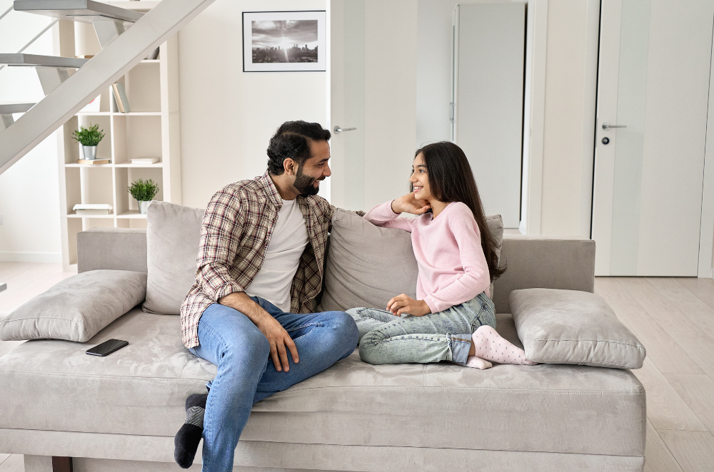 Father sitting with his daughter on a couch, talking to her.