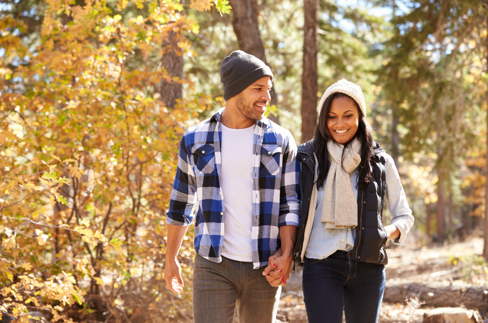 A couple walking together in fall weather with colourful leaves behind them.